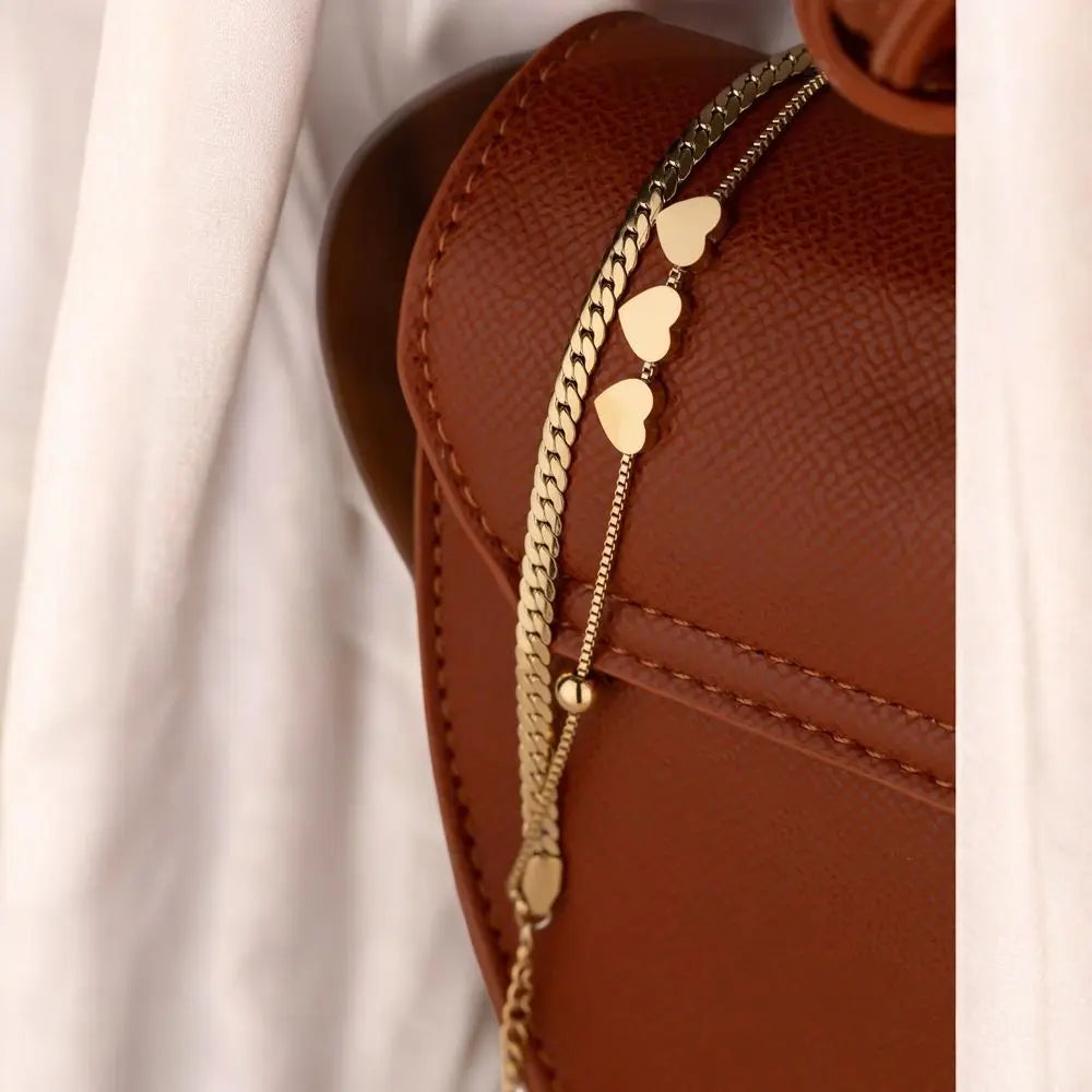 Close-up of a brown leather bag with gold heart-shaped chain detail.