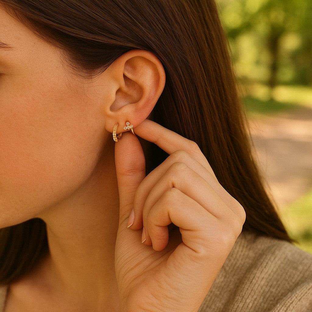 Close-up of a person wearing gold hoop earrings with a blurred natural background