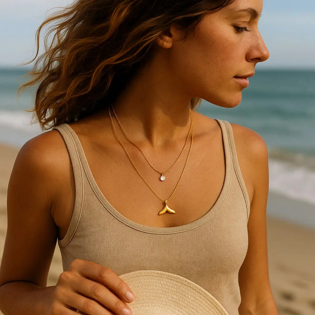 Woman on a beach wearing a beige tank top and gold necklace with a shark tooth pendant.