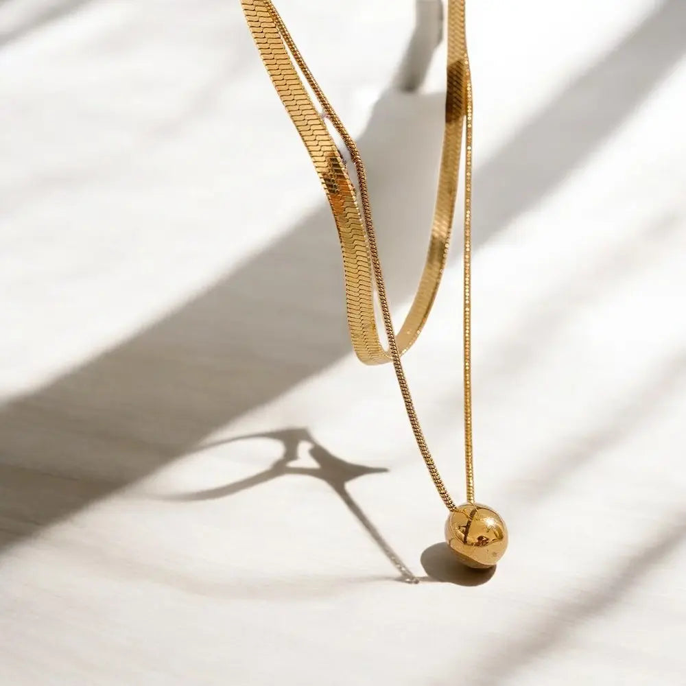Gold necklace with a spherical pendant on a light background