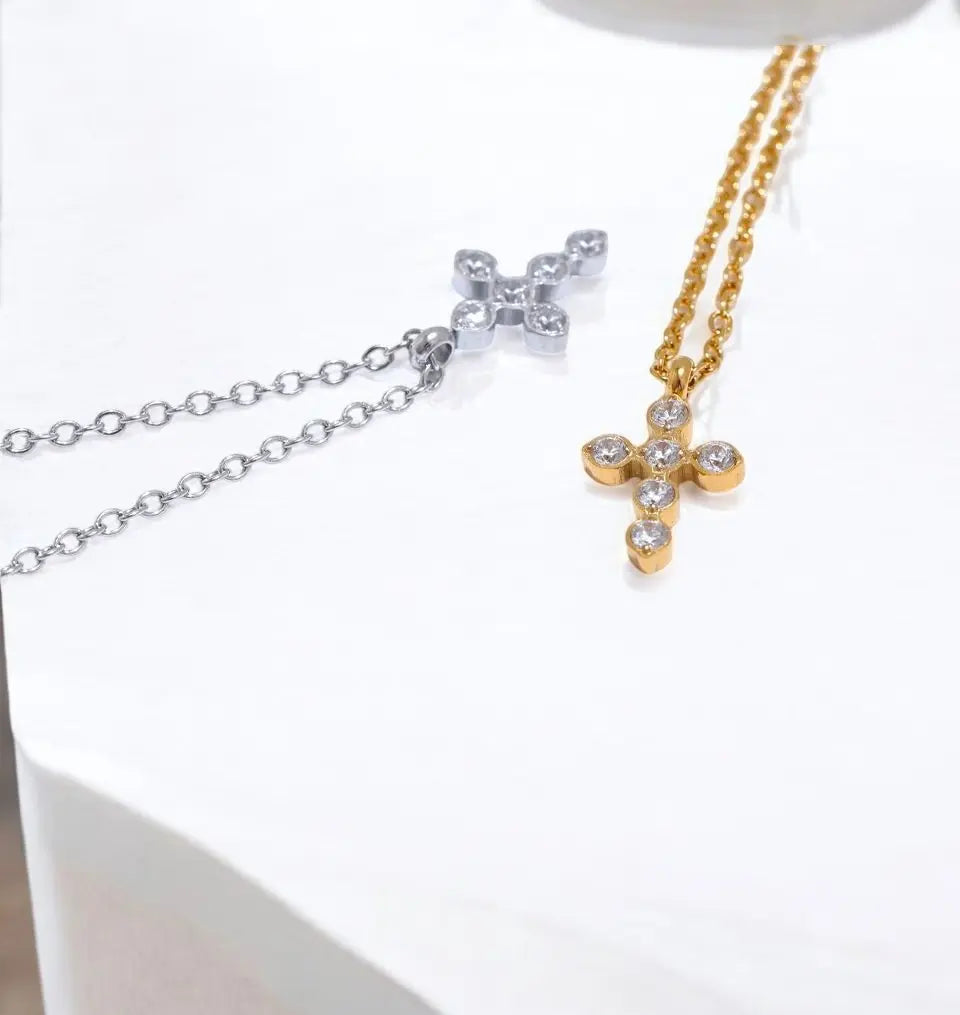 Two cross-shaped necklaces, one gold and one silver, on a white surface.