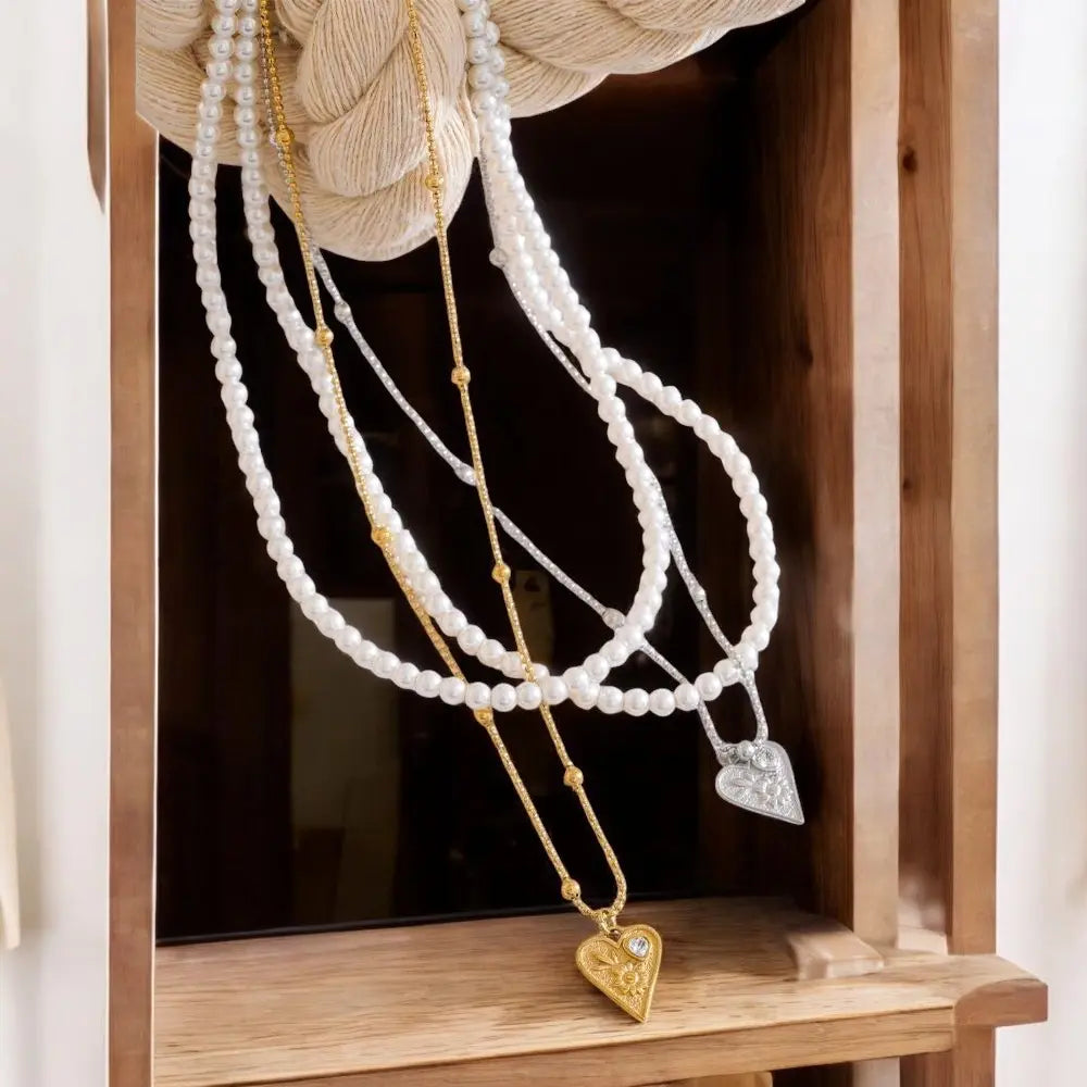Two necklaces with heart pendants on a wooden stand.