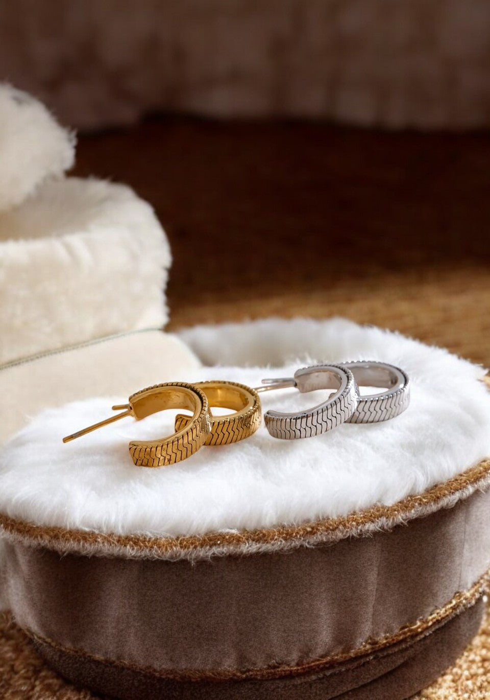 Two pairs of earrings, one gold and one silver, on a white fur surface.