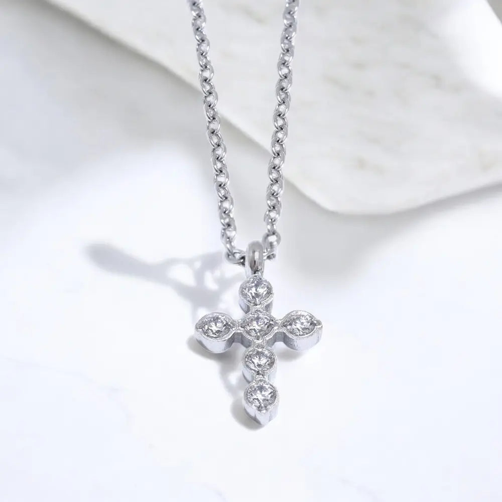 Silver cross necklace with clear stones on a white marble surface