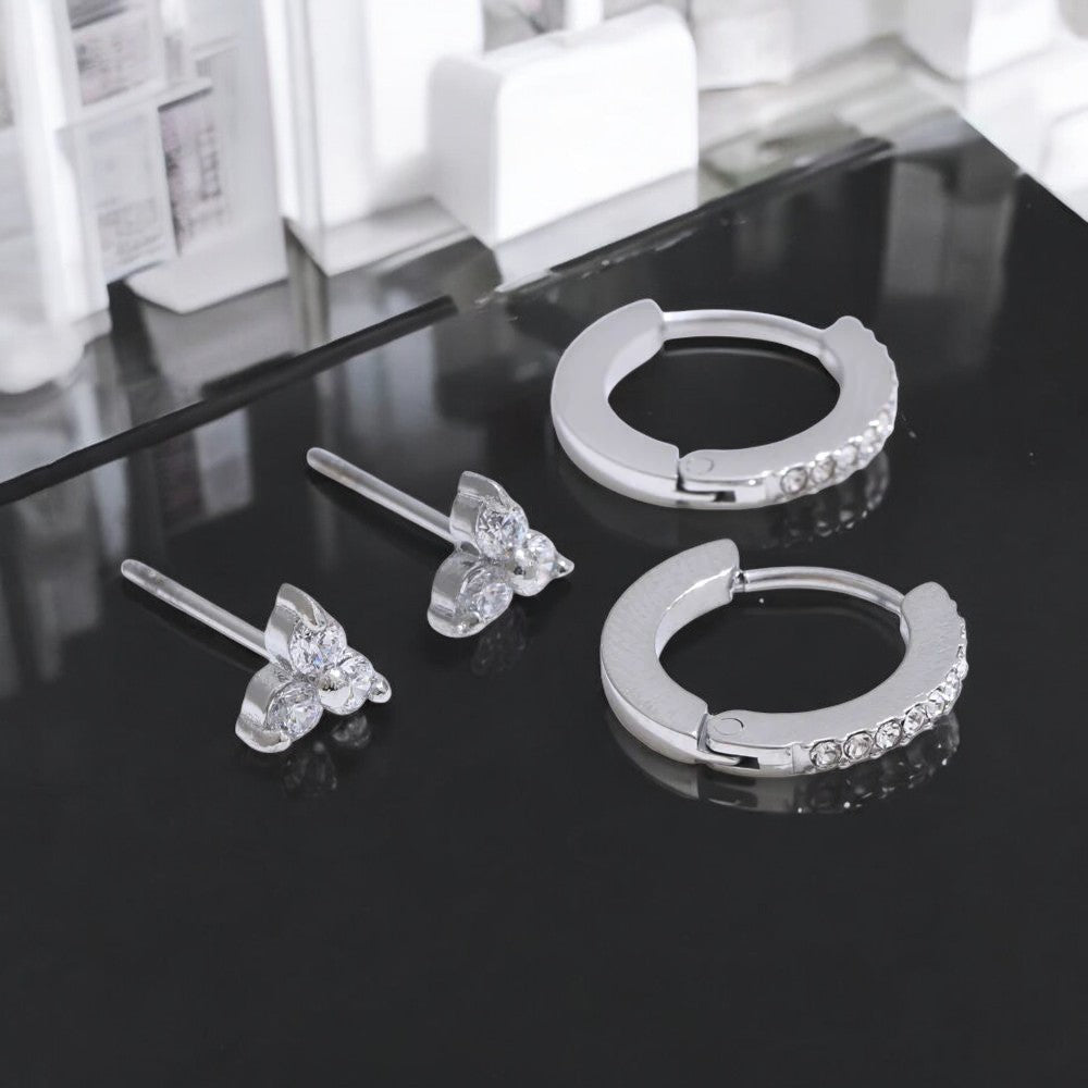 Set of silver butterfly and hoop earrings on a reflective surface