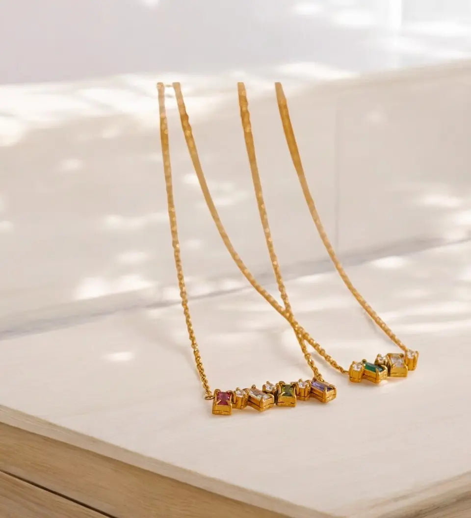 Gold necklaces with colorful gemstones on a light wooden surface