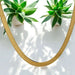 Gold necklace on a white surface with green plants in the background