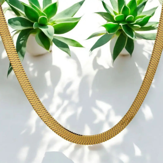 Gold necklace on a white surface with green plants in the background