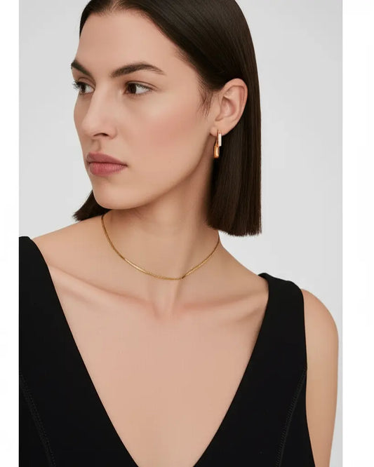 Woman wearing a gold necklace and earrings on a plain background