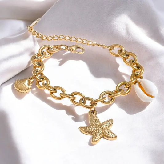 Gold chain bracelet with starfish charm on a white fabric background