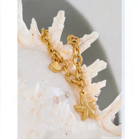 Gold chain bracelet with a starfish charm on a seashell background