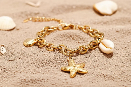 Gold chain bracelet with a starfish charm on a sandy background
