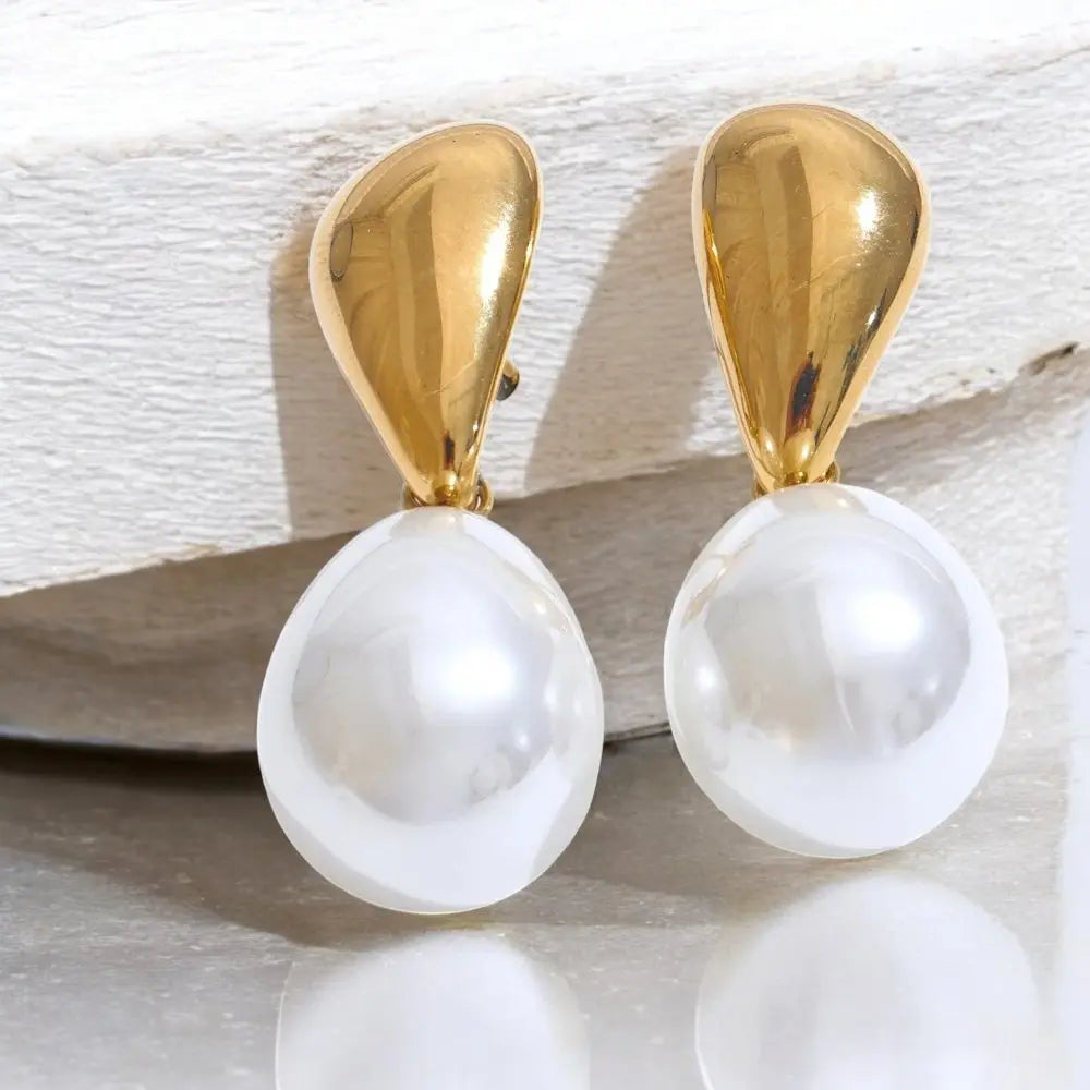 Gold and pearl earrings on a textured surface