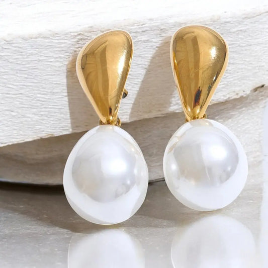 Gold and pearl earrings on a textured surface