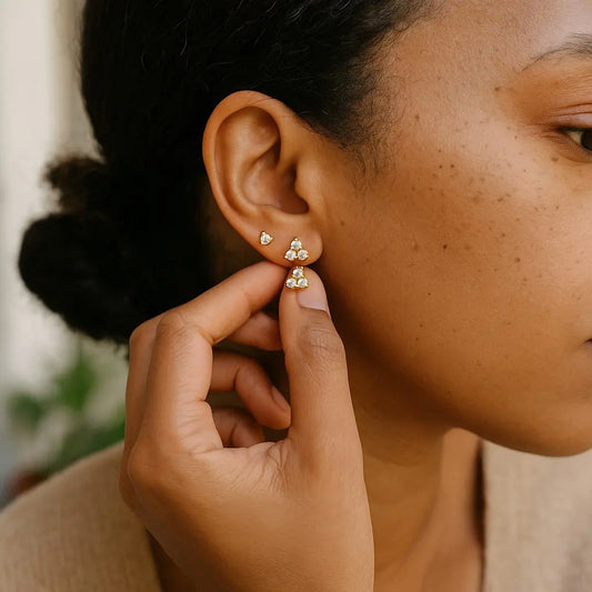 Person wearing a gold earring with three small stones, adjusting it with their hand.