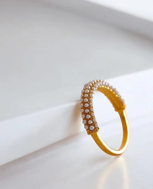 Gold bracelet with pearl-like beads on a white surface