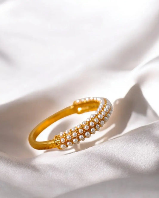 Gold bracelet with pearl accents on a white fabric background