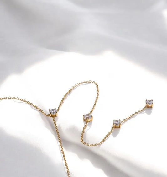 Gold necklace and earrings with clear gemstones on a light background