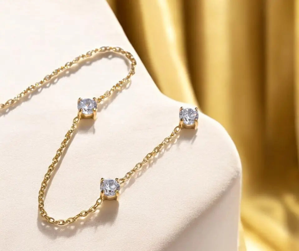 Gold necklace with three clear gemstones on a beige surface
