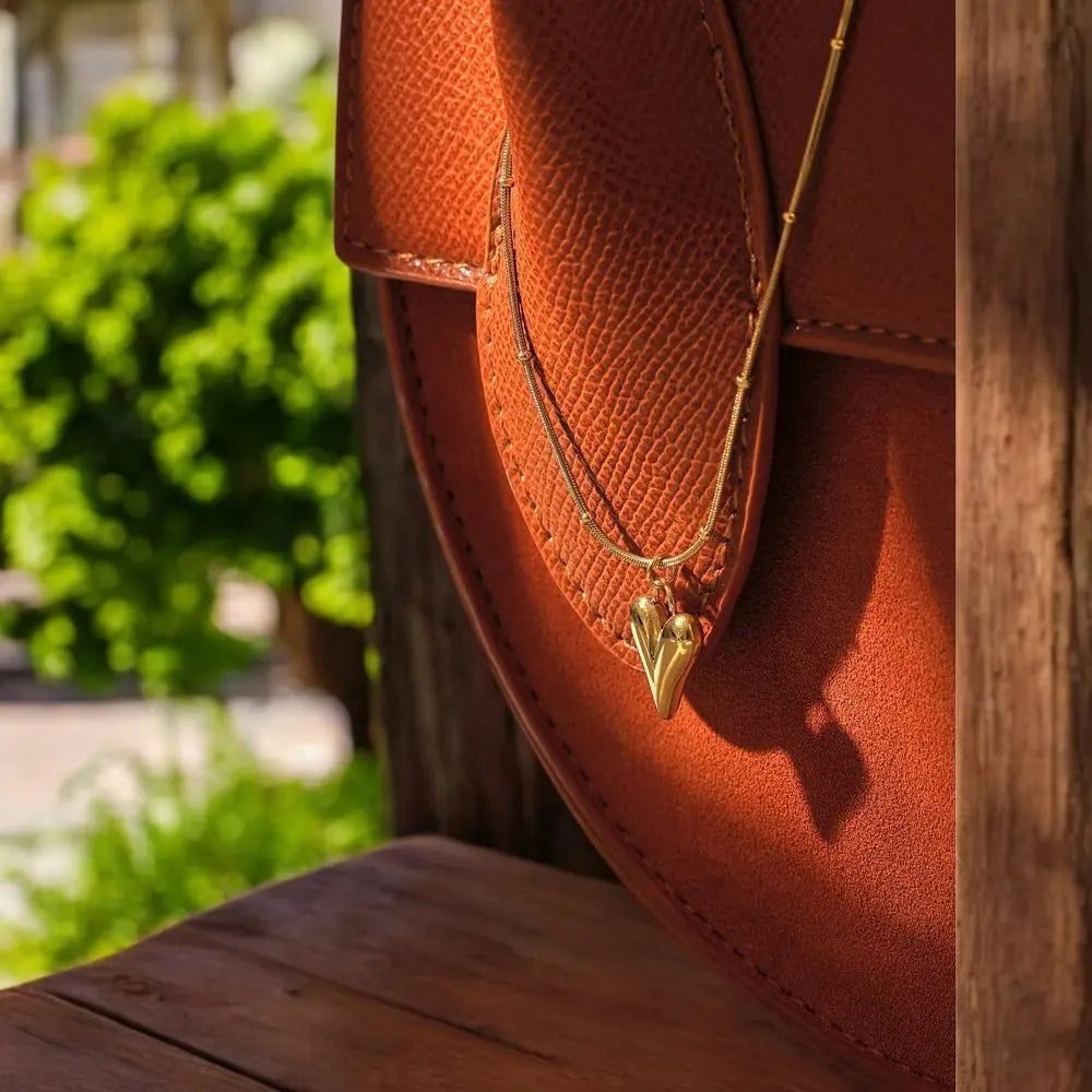 Brown leather loafer with a gold necklace featuring a pendant, outdoors.