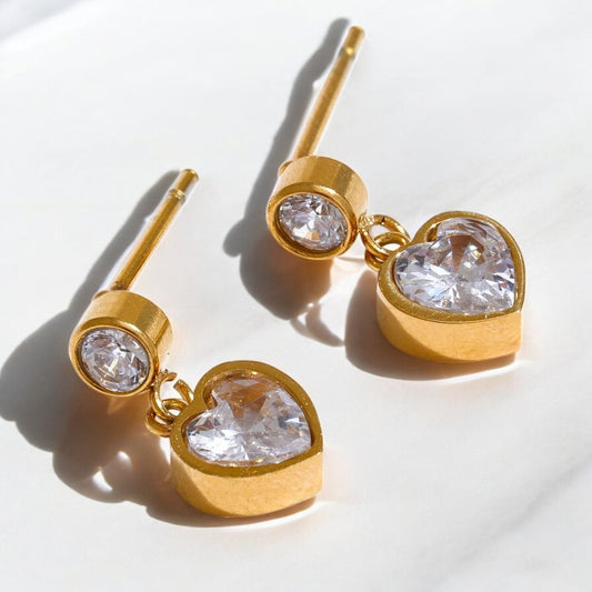 Gold heart-shaped earrings with clear gemstones on a white background