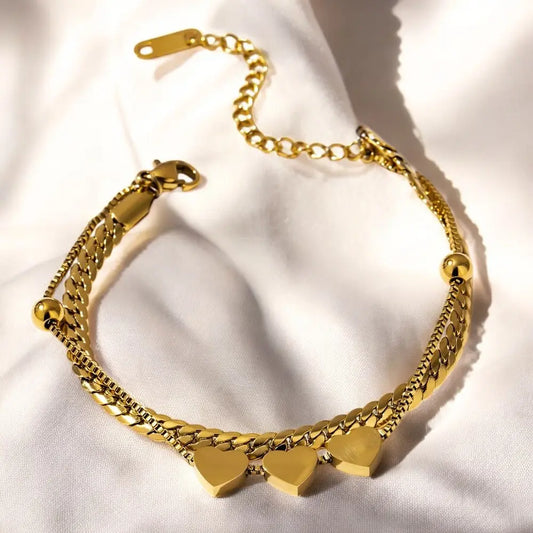 Gold chain bracelet with heart charms on a white fabric background