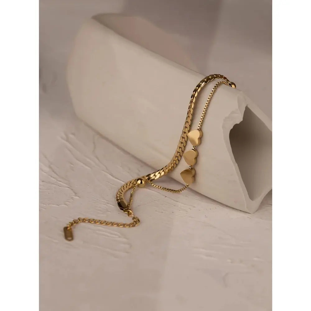 Gold bracelet with heart-shaped charms on a beige surface