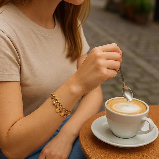 Person stirring a cup of cappuccino with a spoon on a wooden table.
