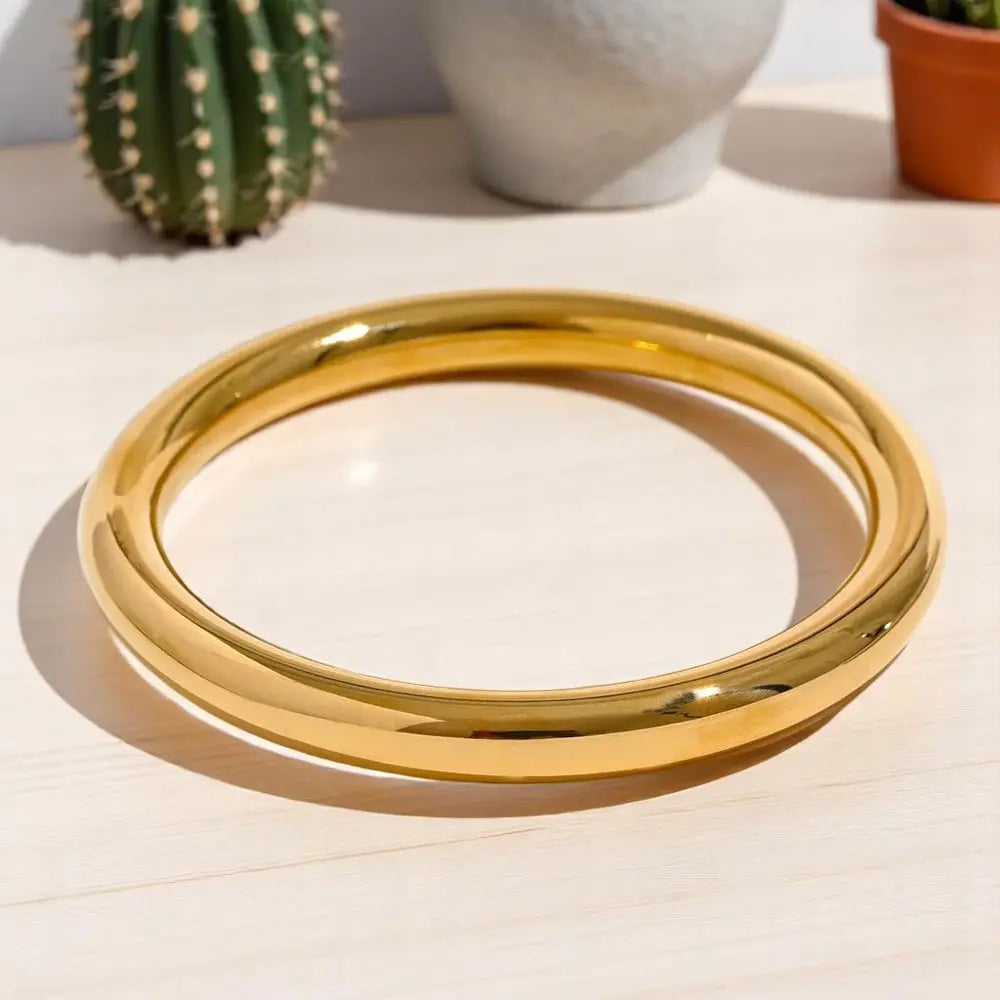 Gold bangles on a light surface with a cactus in the background