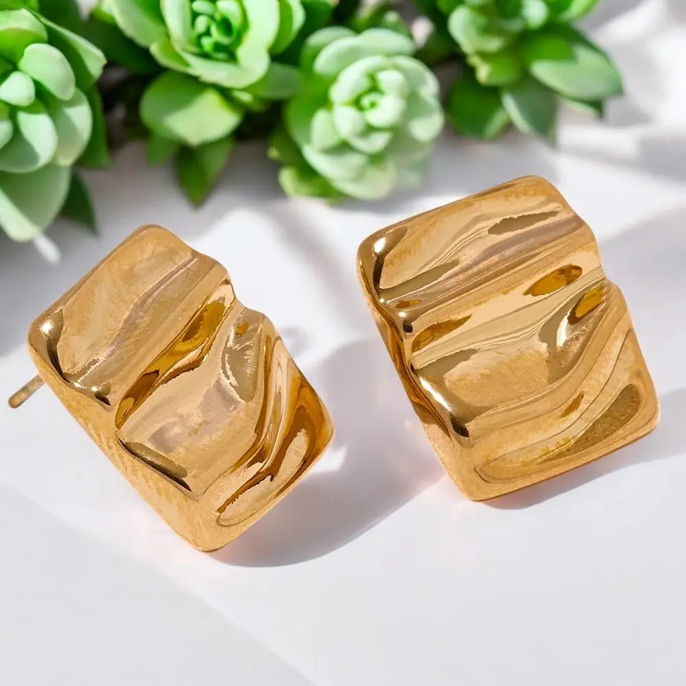 Gold marble-patterned earrings on a white surface with green plants in the background
