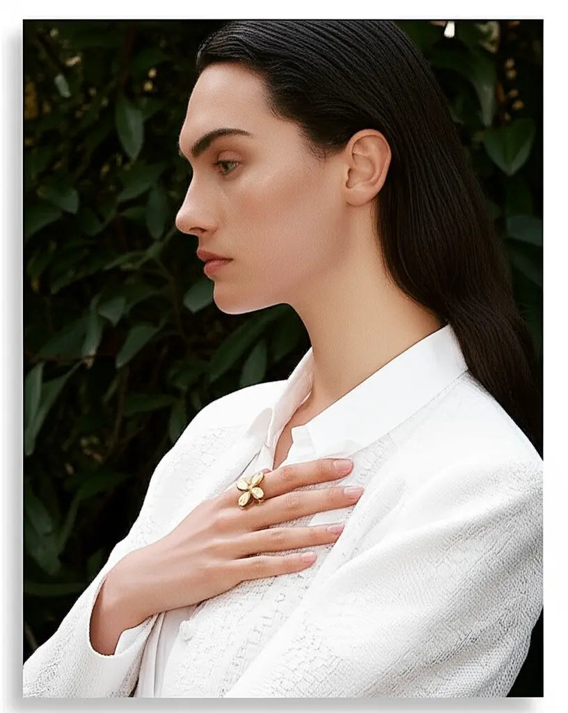 Woman wearing a white garment with a gold ring, standing against a dark green leafy background