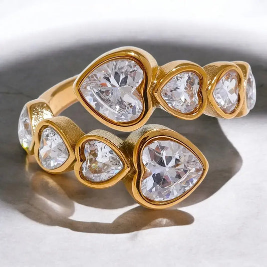 Gold ring with heart-shaped diamond stones on a reflective surface