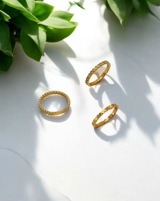 Three gold rings on a white surface with green leaves in the background