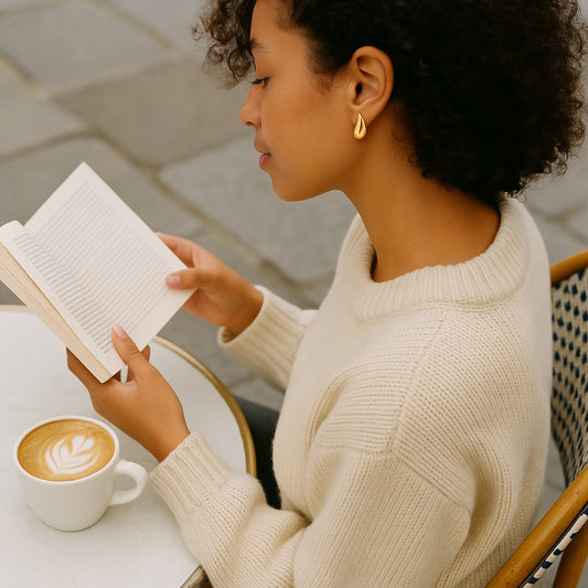 Woman reading a book with a cup of coffee on a table.