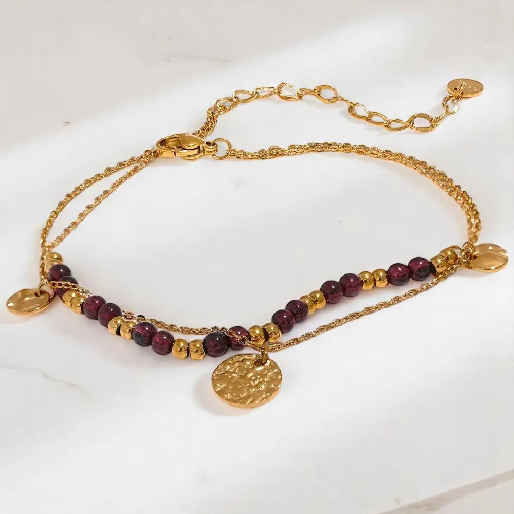 Gold bracelet with red beads and gold coins on a white background