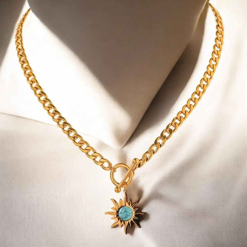 Gold necklace with a sun-shaped pendant featuring a turquoise stone on a white background