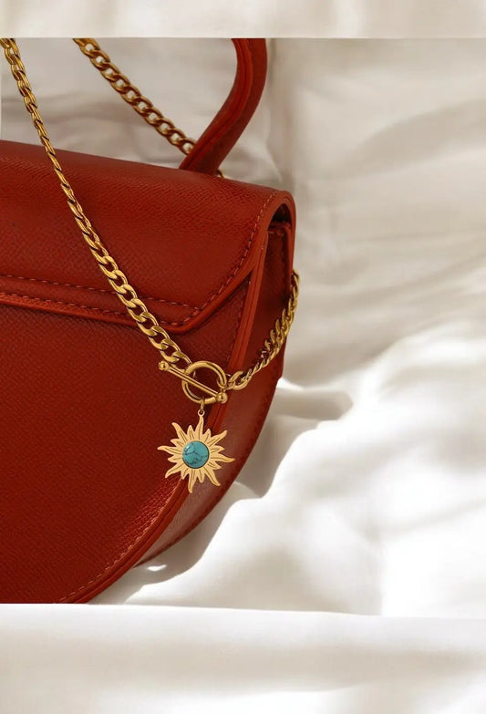 Red handbag with a gold chain and sun-shaped pendant on a white background
