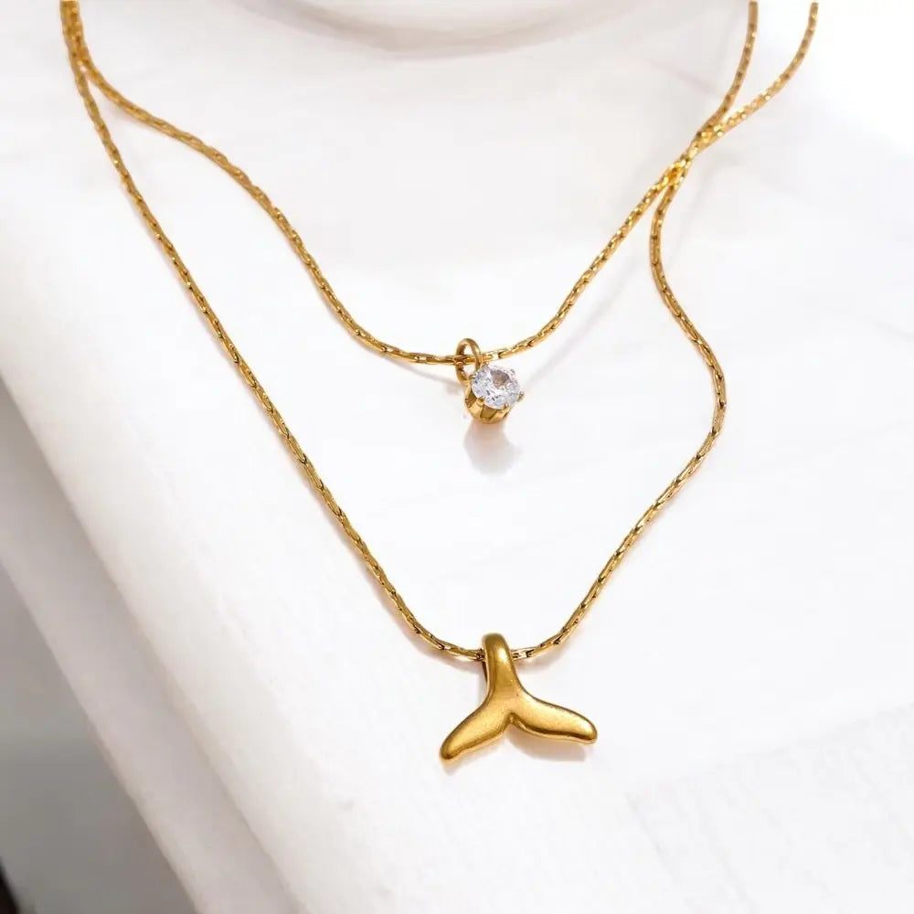 Gold necklace with a whale tail pendant on a white background