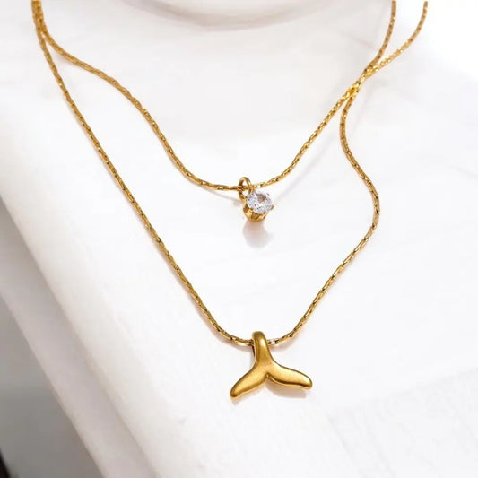 Gold necklace with a whale tail pendant on a white background