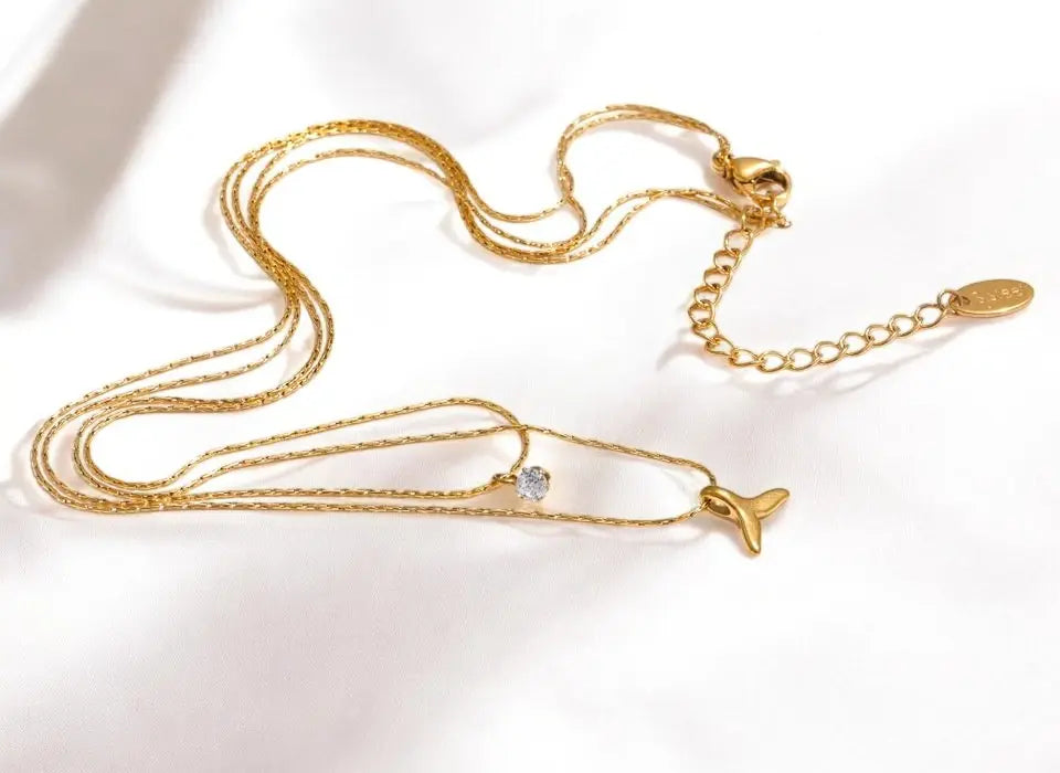 Gold necklace with a whale-shaped pendant on a white background