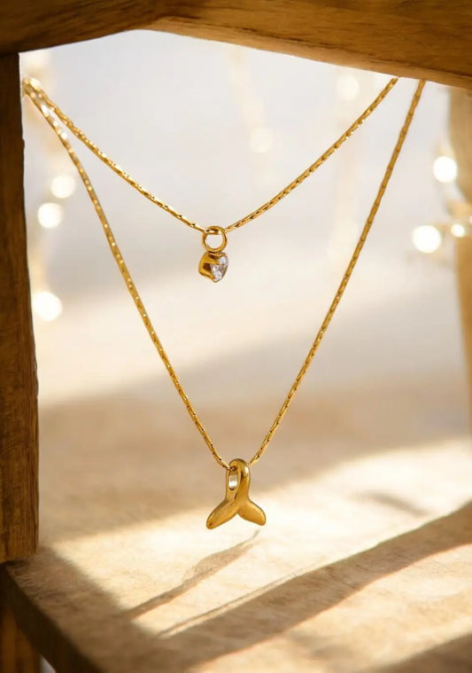 Two gold necklaces with pendants on a wooden surface with soft lighting.