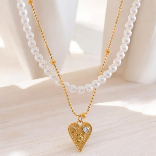 Two pearl necklaces with gold chains and heart pendants on a light background