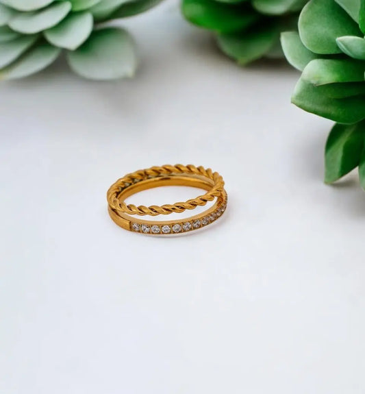 Gold ring with diamond accents on a white surface with green plants in the background