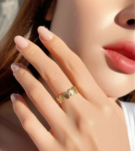 Close-up of a hand wearing a gold ring with a shell design, against a blurred background.