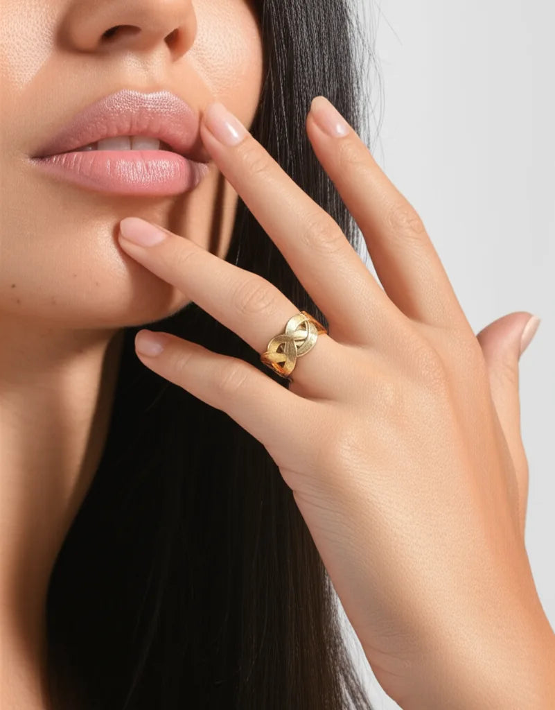 Close-up of a hand wearing a gold ring with a heart design, touching the face.