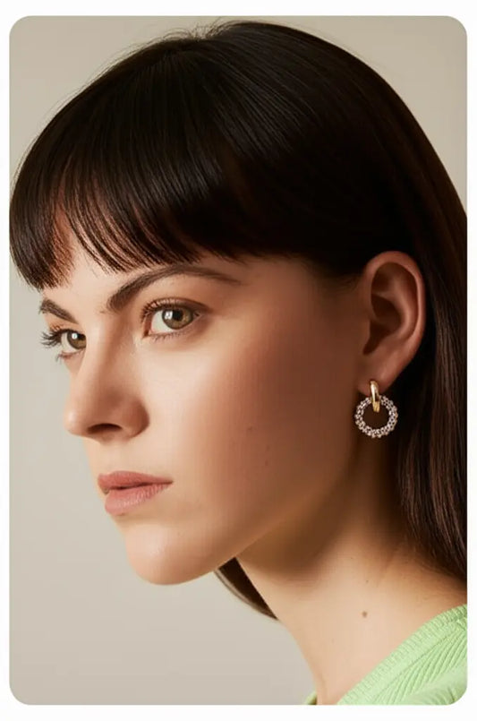 Close-up of a woman wearing gold hoop earrings against a neutral background