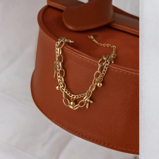 Gold chain bracelet on a brown handbag with a white background