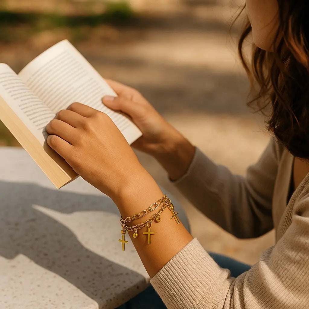 Person reading a book with gold bracelets on a blurred outdoor background