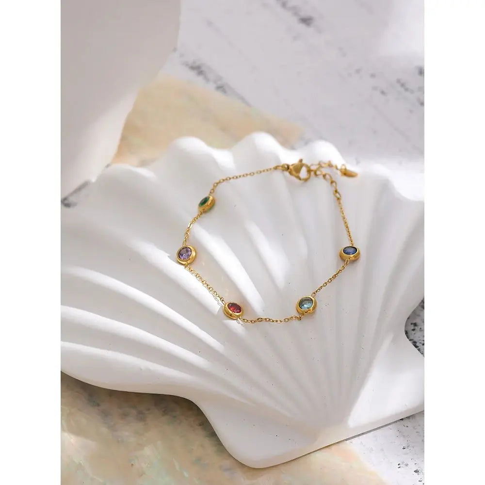 Gold bracelet with colorful gemstones on a white shell