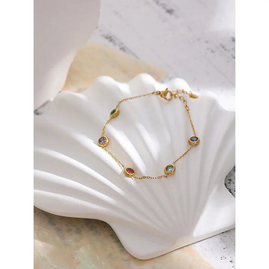 Gold bracelet with colorful gemstones on a white shell